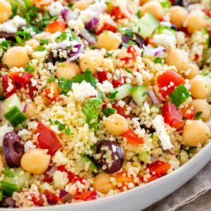 Salade de couscous méditerranéenne Salade de couscous méditerranéen avec une vinaigrette aux herbes fraîches au citron. De minuscules semoules de blé dur cuisent sur la cuisinière, puis sont mélangées à des légumes colorés, du fromage feta, des olives et des pois chiches. Un plat d'accompagnement sain qui a du croquant!