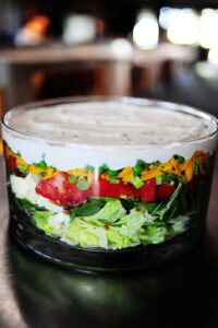 Une salade étagée colorée parfaite pour les repas-partage et les pique-niques. C'est une salade printanière simple et belle, et un aliment de base des repas-partage et des déjeuners dans ma région du pays. Vous pouvez varier les ingrédients selon vos goûts et ce que vous avez dans votre frigo, et vous pouvez l'agrémenter un peu d'herbes fraîches, de gorgonzola, tout ce qui fait voler votre jupe ! Les ingrédients standard de la plupart des salades en couches sont de la laitue ou des épinards (ou les deux !), Des œufs durs, du bacon émietté, du fromage râpé, des oignons verts et des pois verts, qui sont disposés en couches dans un joli bol en verre afin que les couches puissent être vues dans tous les sens. leur beauté colorée.