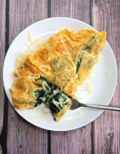 Une omelette délicate et moelleuse est faite en fouettant très bien les œufs, comme si vous alliez faire un gâteau. Feuilles d'épinards fraîches, fromage Cheddar sur le dessus et qui se soucie qu'il ne se plie pas parfaitement