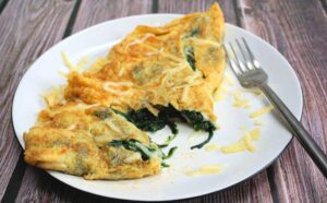 Une omelette délicate et moelleuse est faite en fouettant très bien les œufs, comme si vous alliez faire un gâteau. Feuilles d'épinards fraîches, fromage Cheddar sur le dessus et qui se soucie qu'il ne se plie pas parfaitement